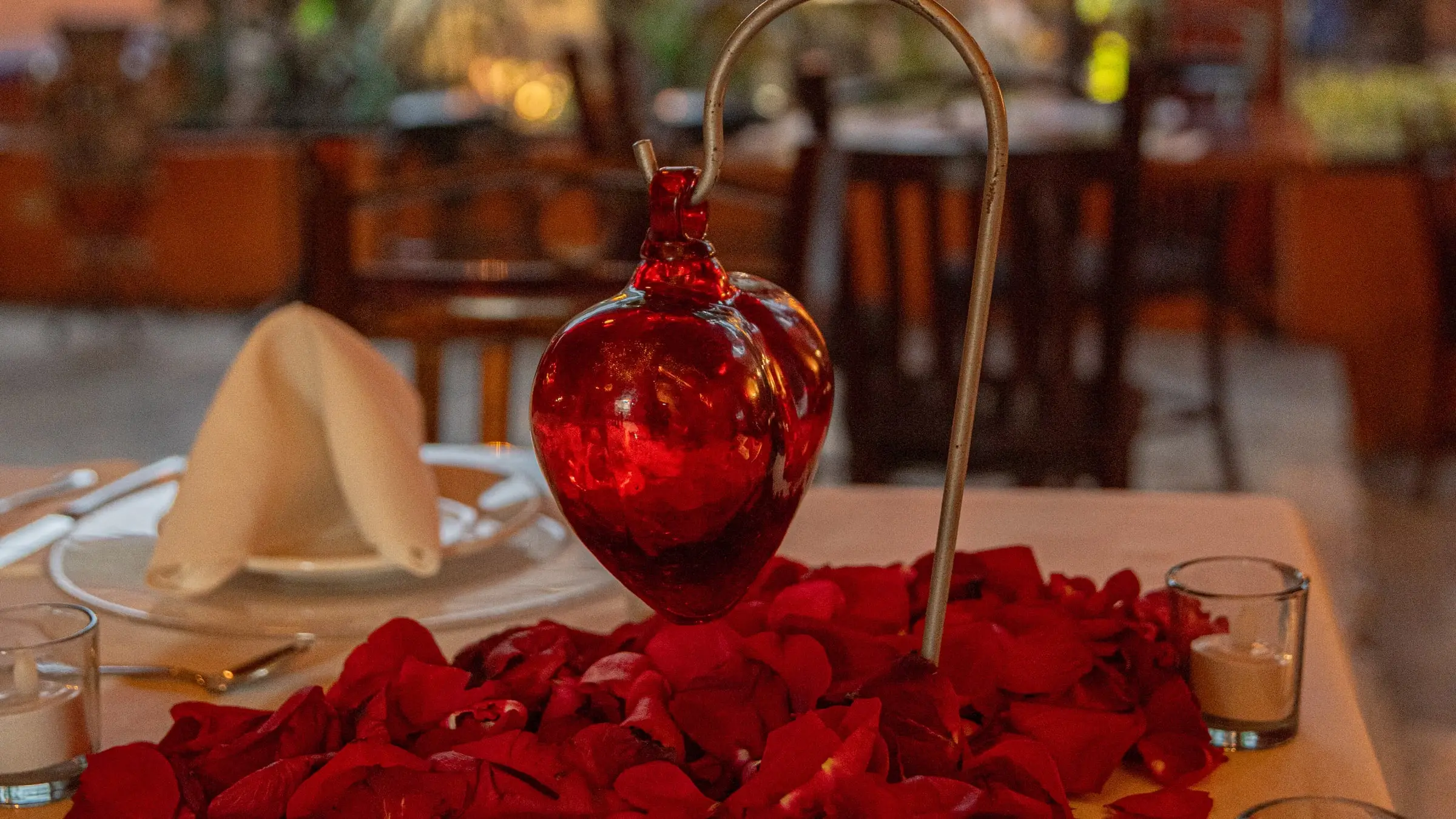 El corazón de cristal soplado sobre los pétalos de rosa, con la mesa para dos ya puesta