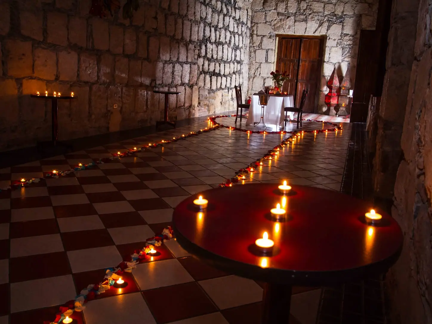 Camino de velas sobre el piso de ajedrez del Salón Romancera, con la mesa iluminada al fondo